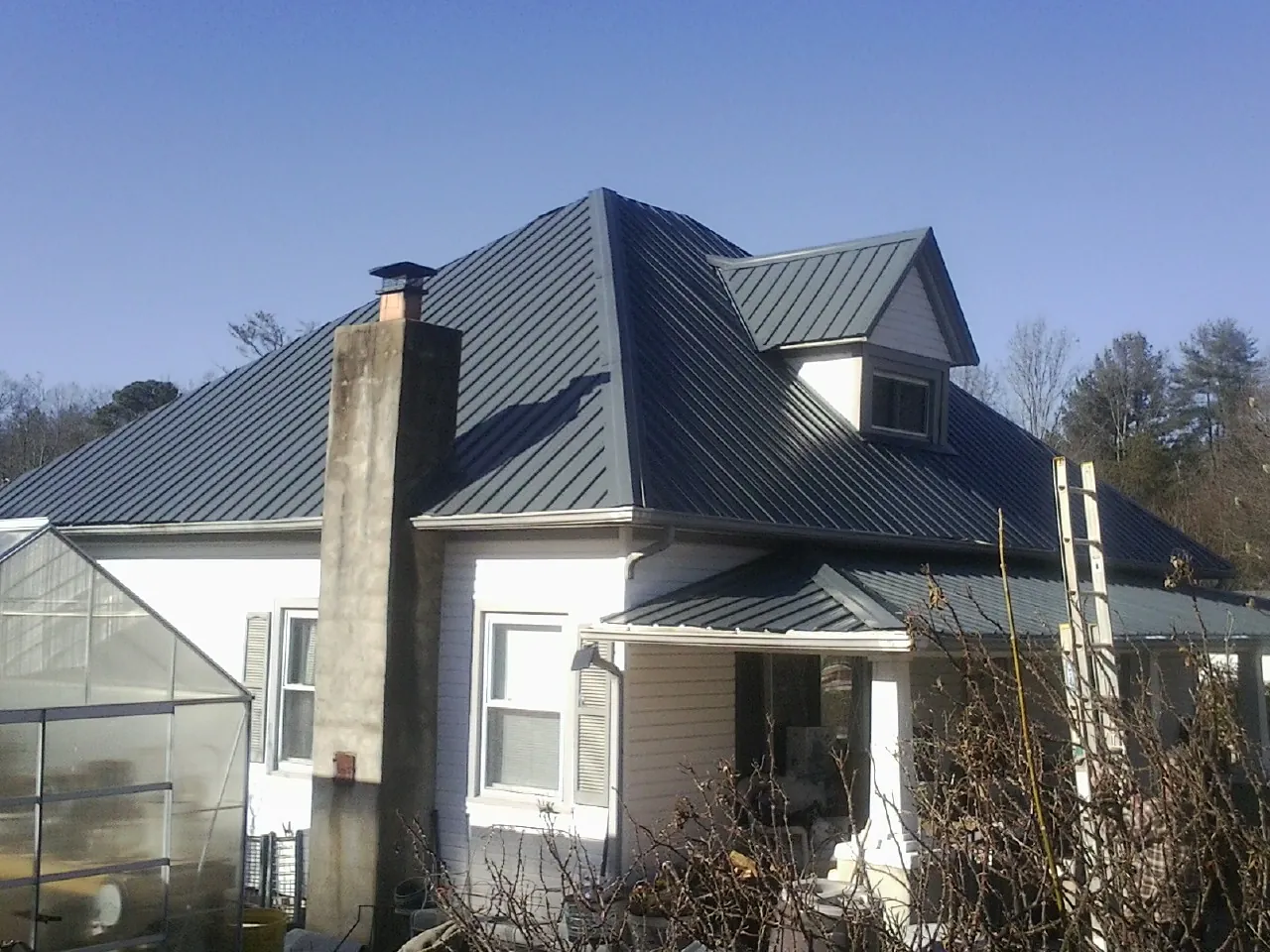 Dark blue standing seam metal roof on a white farmhouse with dormer — Slate & Tile Roof Repair by Roofing Brothers in Grand View