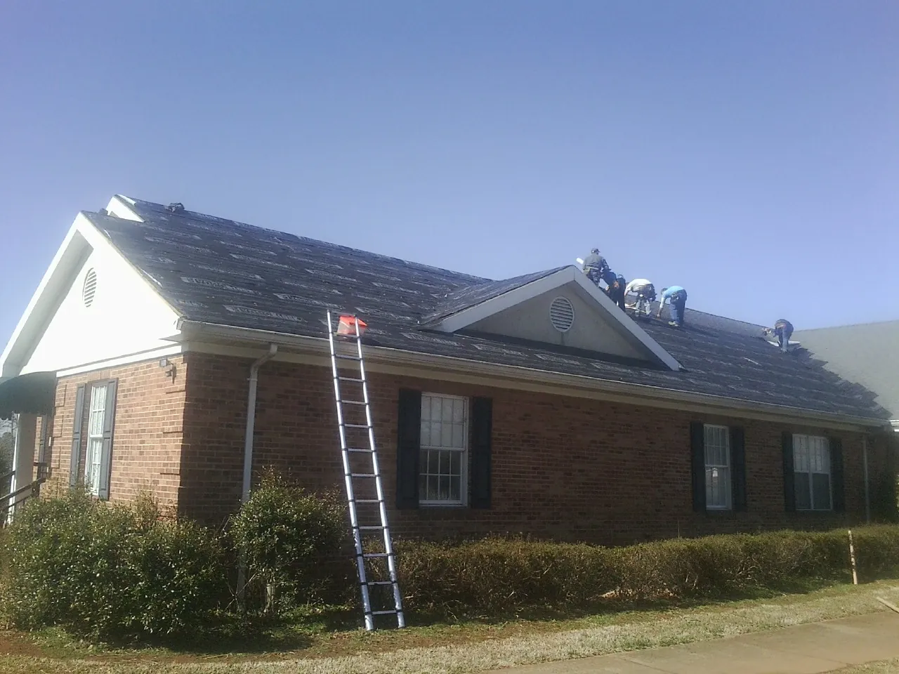 Crew tearing shingles off a brick ranch roof with a ladder set — Emergency Roof Repair work by our crew in Grand View