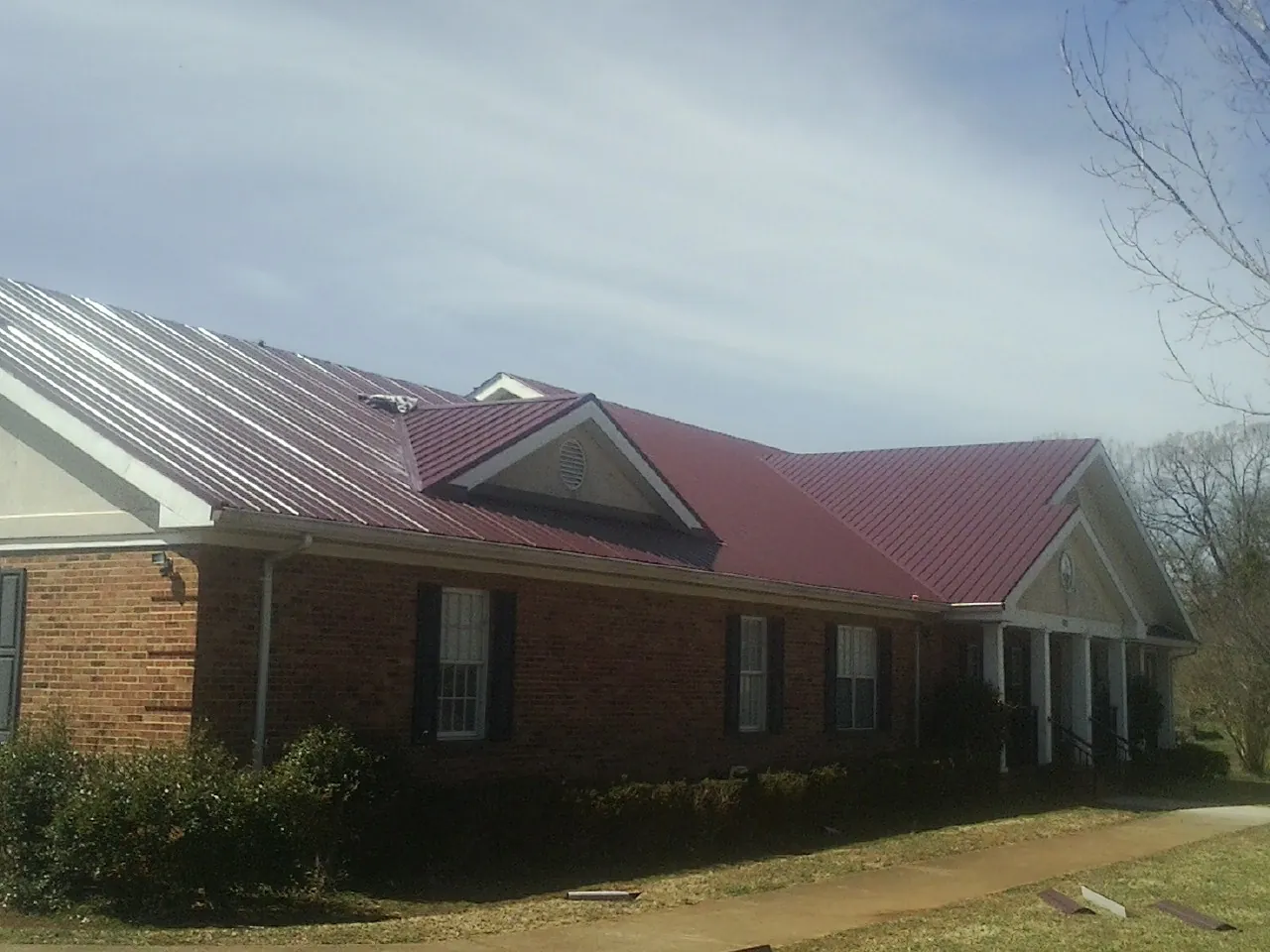 Red metal roof with gabled entries on a long brick building, from a Hail Damage Roof Repair job in Grand View