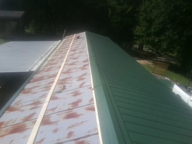 Old rusted panels beside newly installed green metal roofing — Wind Damage Roof Repair by Roofing Brothers in Grand View