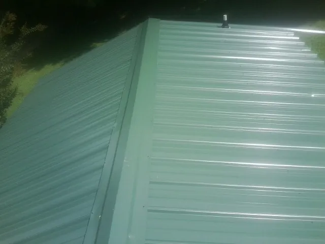 New green metal panels meeting at the ridge of a roof — Flat Roof Repair work by our crew in Grand View