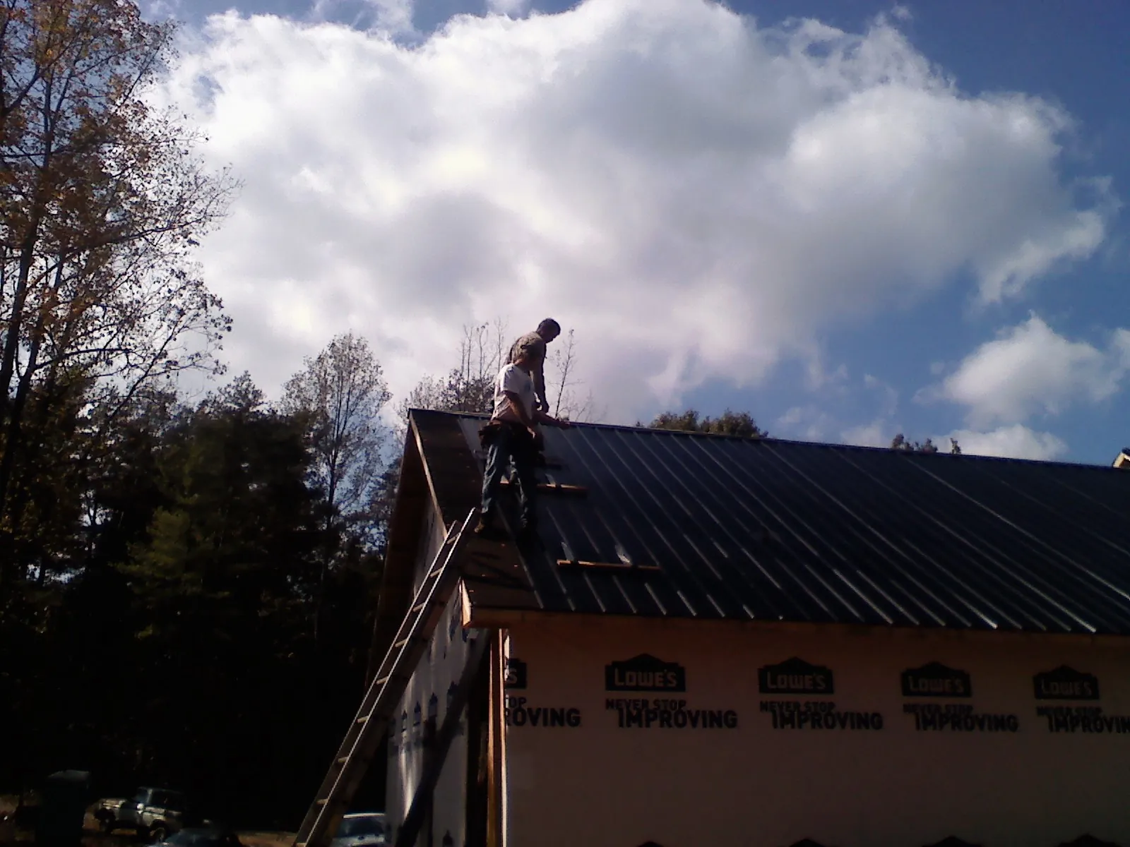 Roofer fastening dark metal panels high against a cloudy sky, from a Roof Inspection job in Grand View