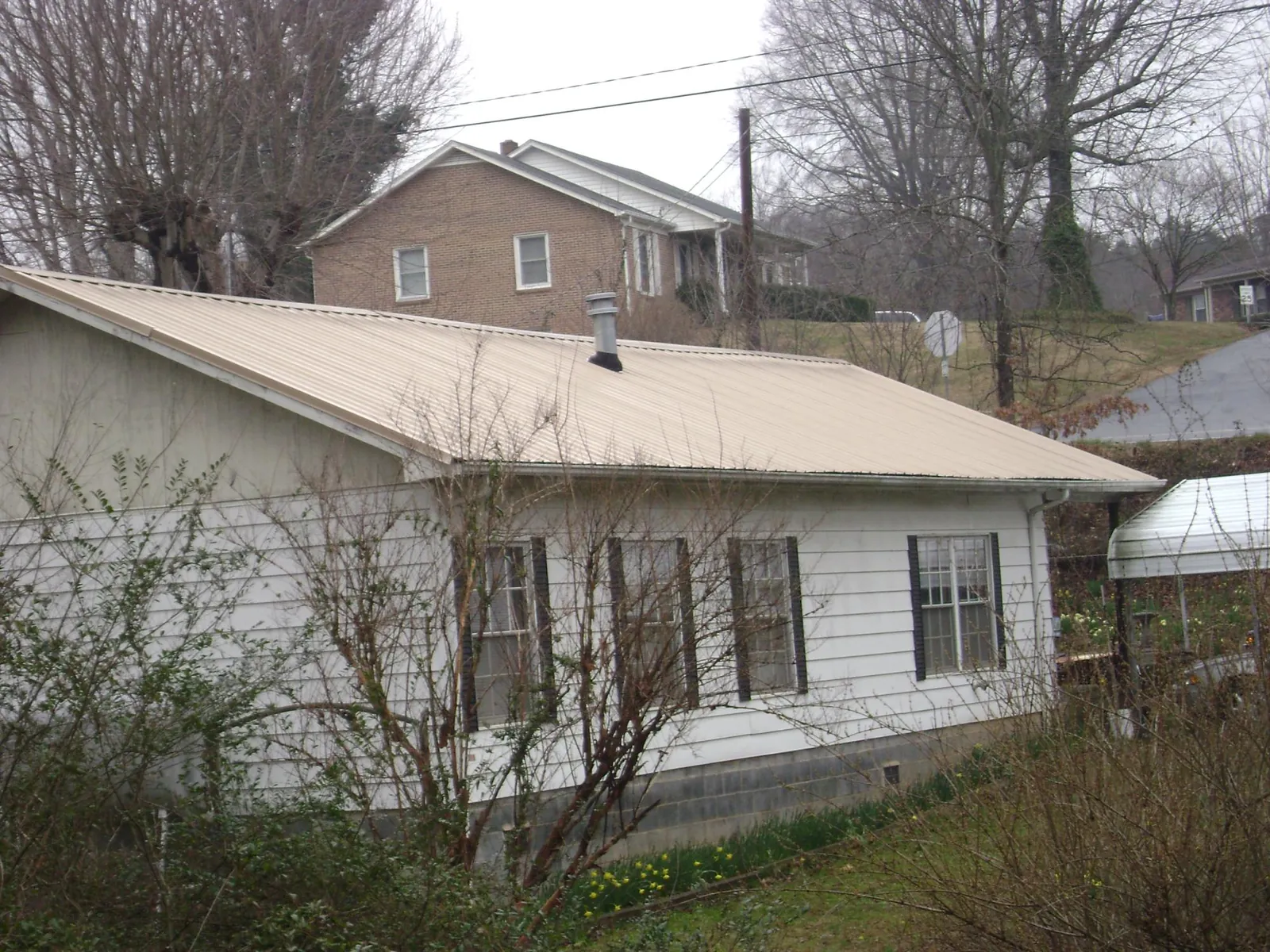 Tan metal roof on a white sided house set into a hillside — Commercial Roofing by Roofing Brothers in Grand View