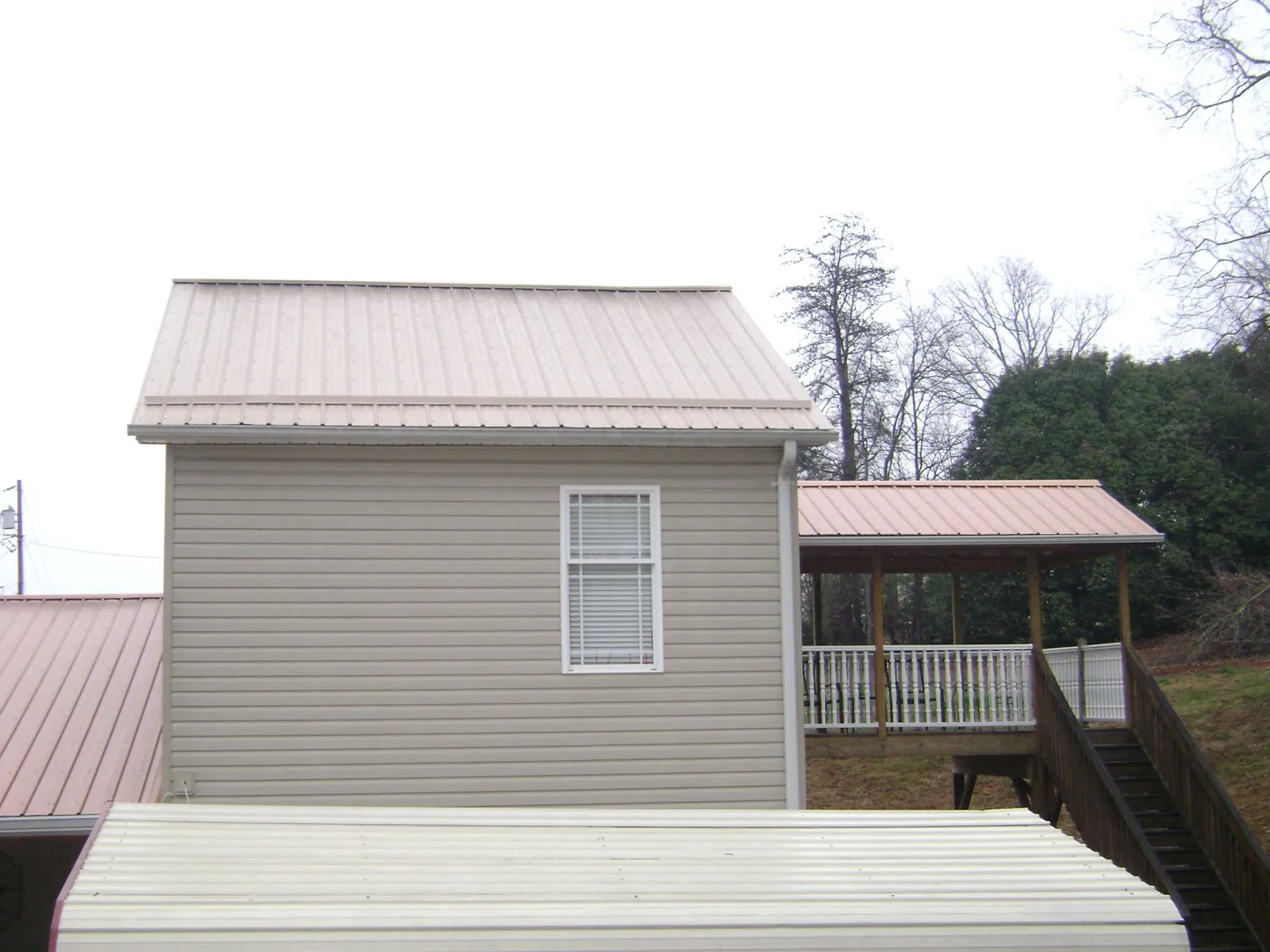 Tan metal roofs on a two story addition and attached porch, from a Roof Replacement job in Grand View